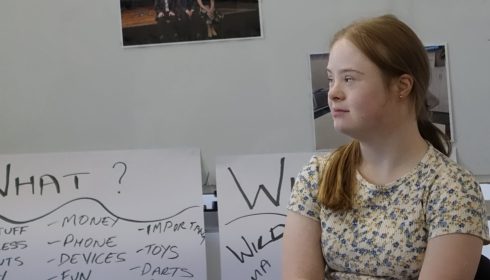 Image of a young woman sitting in front of a whiteboard with posters