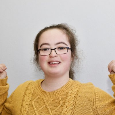 A young woman in a yellow shirt raises her hands