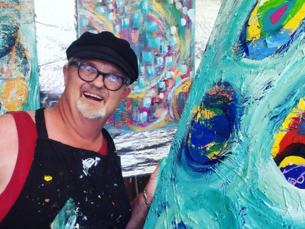 A man stands next to his colourful artwork