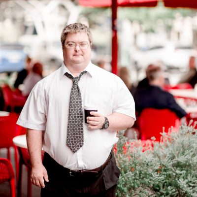 A man a work shirt and tie holding a coffee