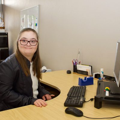 A young woman sitting at a desk next to a computer