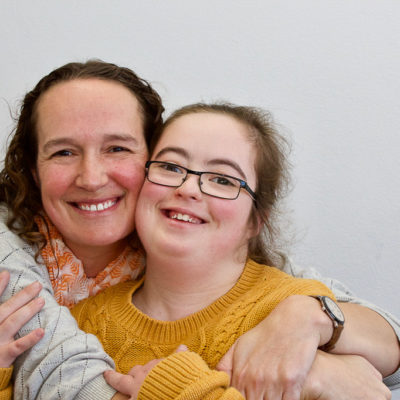 Two women stand together with arms around each other