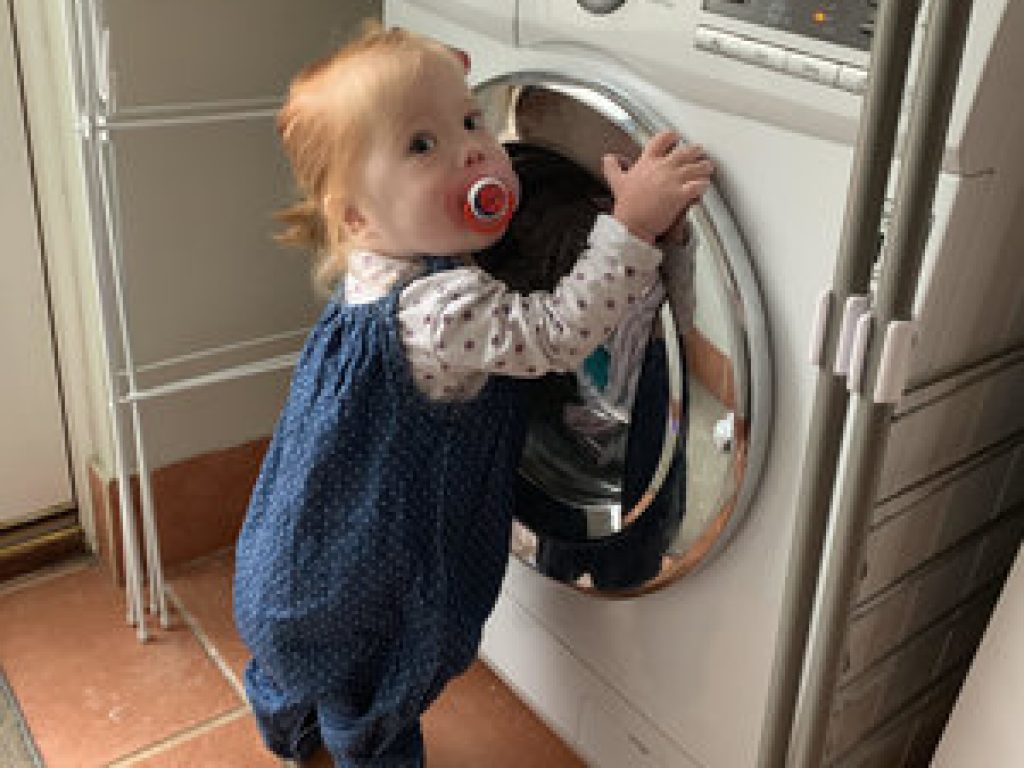 Baby standing next to a washing machine.