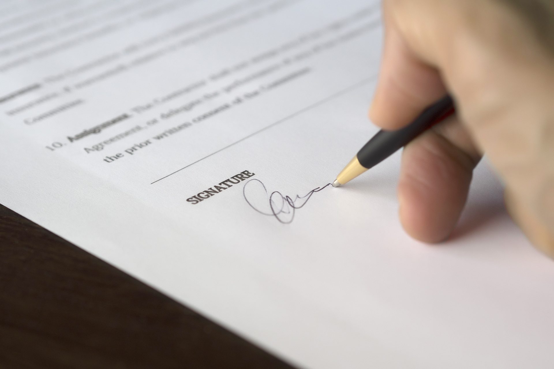 A close up photo of a hand holding a pen writing a signature on a contract