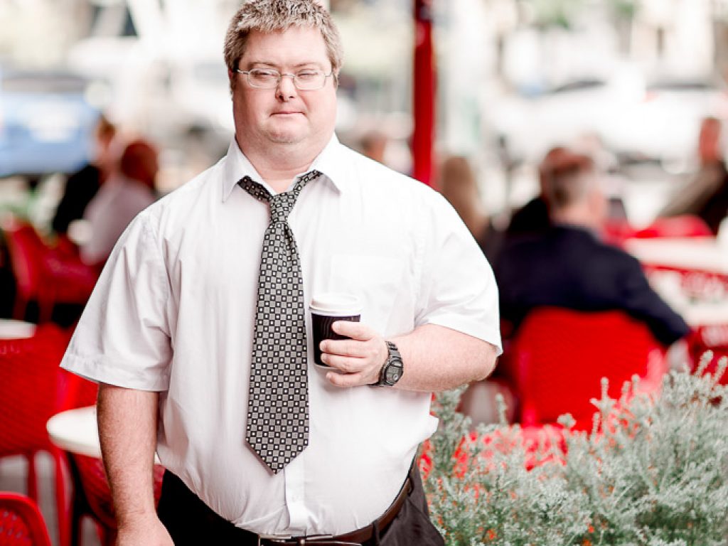 A young man in a work shirt holds a cup of coffee